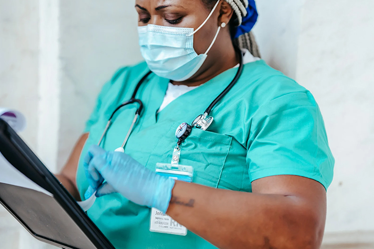 An aesthetic nurse wearing a mask and scrubs checking a patient’s records