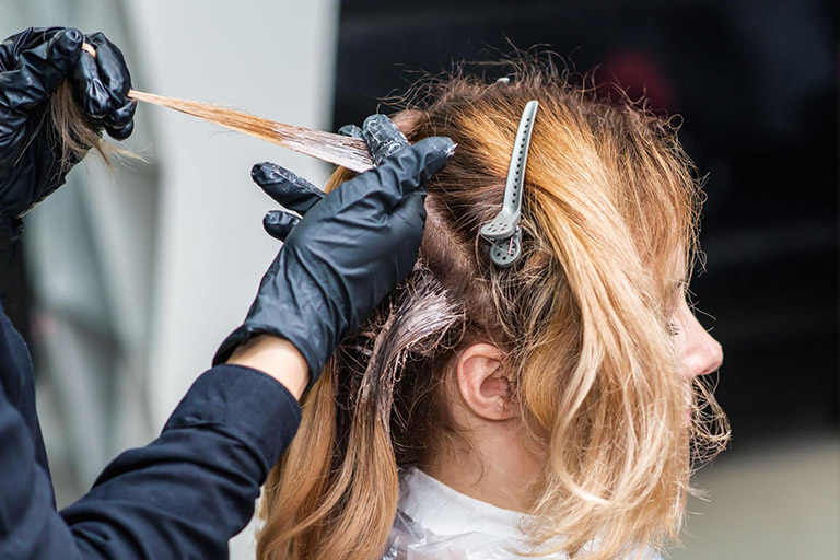 A hair specialist dyeing a woman’s hair in a salon