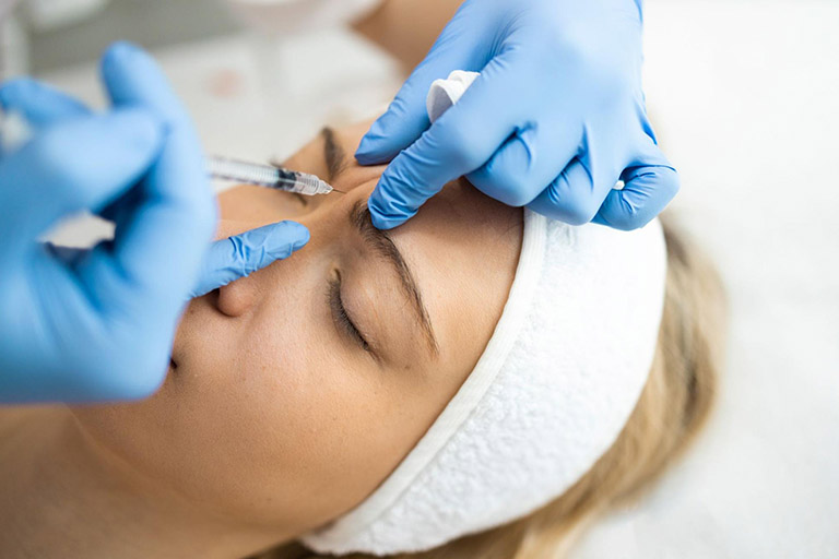 An aesthetician injects Botox between the eyebrows of a female patient