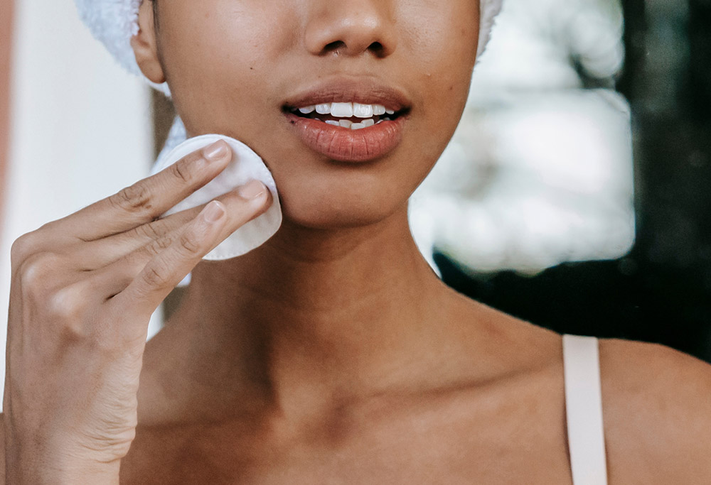 A woman cleansing her face with a cotton wipe