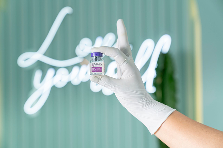  A small bottle of Botox held up in front of a neon “Love Yourself” sign
