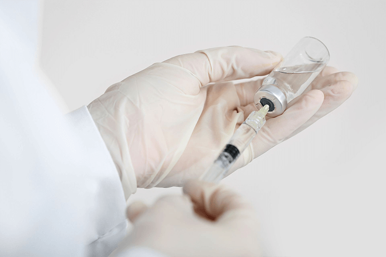 A clinician using a syringe to collect substance from a bottle 