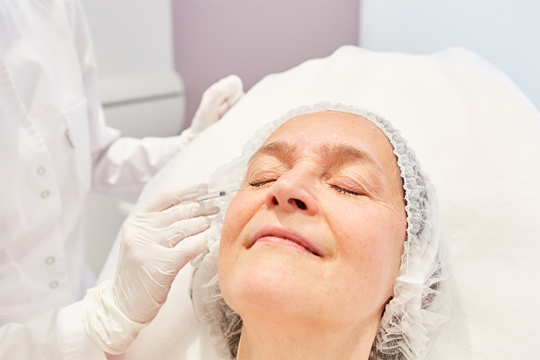 An aesthetic practitioner administering dermal fillers around the mouth on a middle-aged patient
