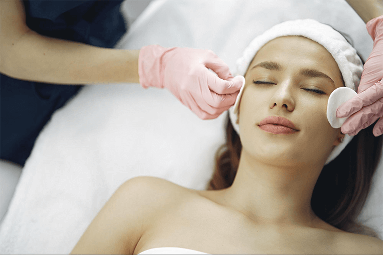 Woman getting a facial treatment from a woman wearing pink gloves 