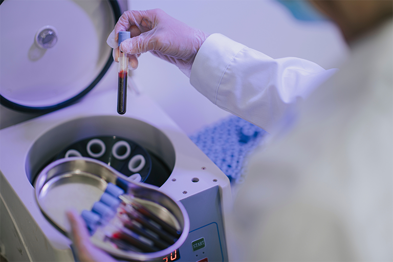  A medical technician putting vials of blood samples in a centrifuge machine 